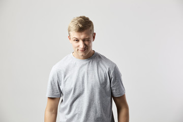 Winking blond guy dressed in a white t-shirt stands on the white background in the studio