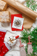 Christmas composition on a white fluffy rug view from above. A cup of hot chocolate and marshmallows, festive decor, knitted sweater, greeting card. Christmas light background