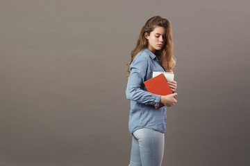 Brown-haired girl dressed in a white t-shirt, jeans and jeans holds books in her hands on a gray background