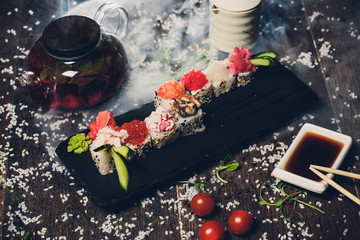various sushi on white plate with chopsticks on wooden background.