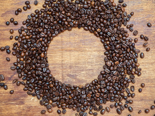 Top view of circle made of roasted coffee beans on wooden background, copyspace, flat lay