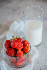 A Cup with fresh ripe strawberries and a glass of milk.