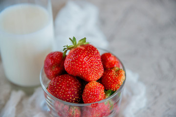 A Cup with fresh ripe strawberries and a glass of milk.