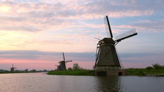 Fascinating view of Alblasserwaard polder with traditional Dutch windmills against setting sun shining through clouds on background. Beautiful rural scenery at sunset. Knderdijk, Netherlands.