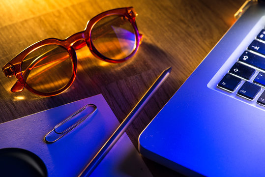 Notebook, pencil, glasses and computer in red and blue light.