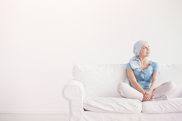 Happy teenage girl suffering from breast cancer, wearing blue headscarf and siting cross leg on the...
