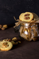 Healthy vegan homemade handmade cookies with walnuts in glass jar on brown background closeup with sugar powder spinkled