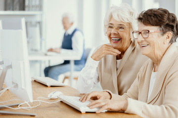 Two smiling senior women with glasses during computer classes for elderly people