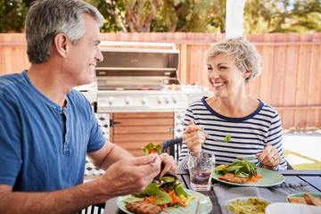 Senior white couple eating together at a table in the garden