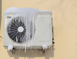 The conditioner covered with icicles on a yellow wall