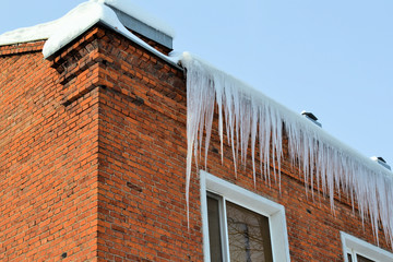 Long, big and dangerous icicles on a brick house roof