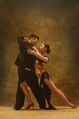 The young dance ballroom couple in gold dress dancing in sensual pose on studio background. Professional dancers dancing tango. Ballroom dance concept. Human emotions - love and passion