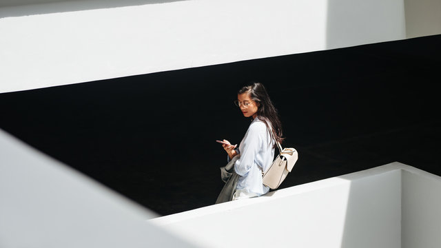 Beautiful Thai woman standing between the building floors and typing on her cell phone.