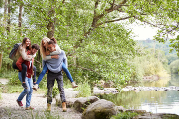 Four adult friends during a hike, men piggybacking their girlfriends