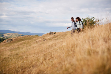 A mixed race young adult couple smile while walking across a field downhill during a mountain hike