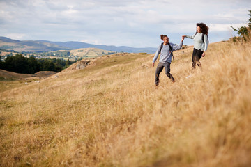 Naklejka na ściany i meble Mixed race young adult couple holding hands while walking walking down a hill during a mountain hike