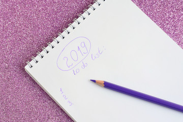 New year 2019 to do list with in spiral paper album. color violet pencil with selective focus and notebook on shiny sparkle glittery pink background with bokeh lights. back to school.