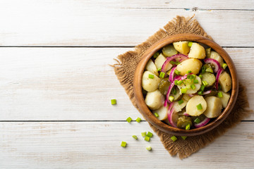 Potato salad with pickled cucumbers and onion in bowl on white wooden table. Top view. Copy space.