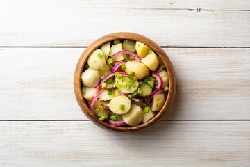 Potato salad with pickled cucumbers and onion in bowl on white wooden table. Top view. Copy space.