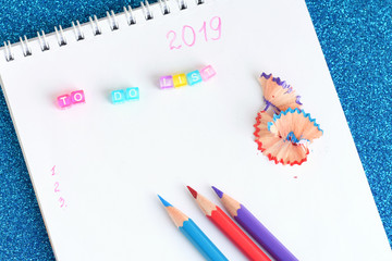 New year 2019 to do list in spiral paper album with colorful letters. color pencils red, blue, violet with selective focus and notebook on shiny sparkle glittery blue background. back to school.