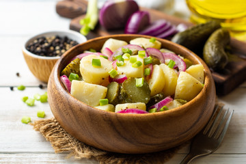 Potato salad with pickled cucumbers and onion in bowl on white wooden table. Selective focus.