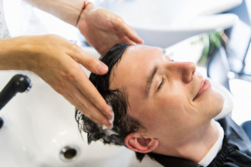 Profile view of a young man getting his hair washed and his head massaged in a hair salon.