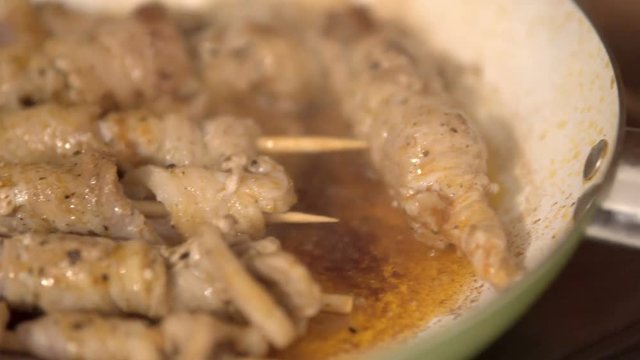 Frying a pork skewers in pan on gas stove, made of white meat and bacon