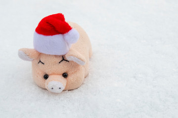 Toy pink pig red Santa Claus hat on white snow. The concept of the New Year and Christmas. Copy space.
