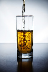 Natural drink of dark yellow color is typed in a glass on a lighted background.