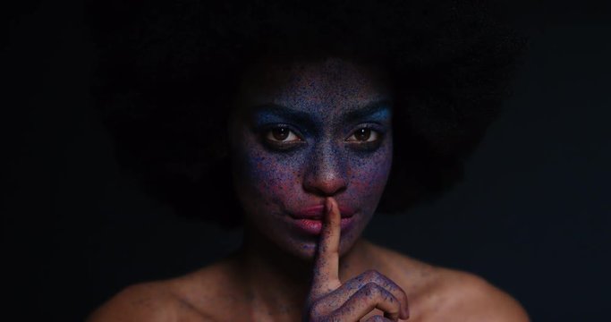 portrait beautiful african american woman wearing face paint body art showing silence gesture mysterious female keeping secret light flashing in dark background creative expression concept