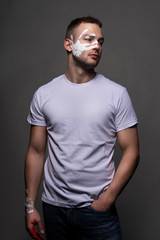 Stylish athletic male artist wearing a white t-shirt stained with red paint posing on gray background. White handprint of the palm on his face. Conceptual, fashion design. Copy space.