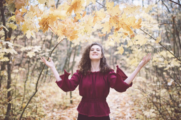 Happy girl in an atumn park throwing maple leaves