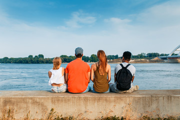 Rear view diverse group of friends chill out on the city river bank.