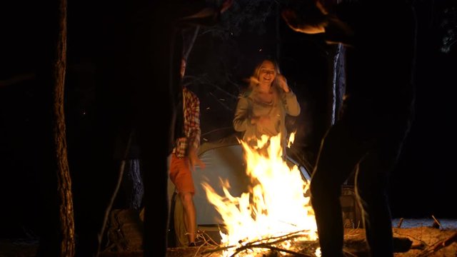 Joyful people dancing around fire in woods at night, party with friends, ritual