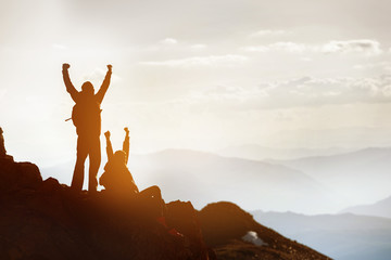 Two happy silhouettes tourists at mountain top success win