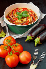 Traditional French quiche in the baking dish with vegetables on the black wooden background. Vegetarian tart decorated with fresh eggplants, tomatoes and basil leaves. Side view