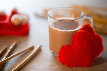 Cup of hot cocoa, two hearts and sweet sticks on a table with a blurred background. Holiday atmosphere.