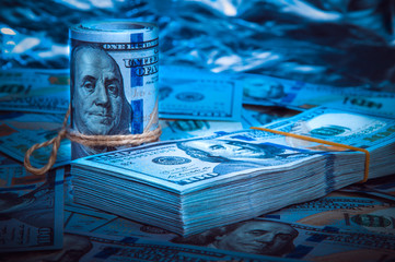 A roll of dollars with a pack of dollars against a background of scattered hundred dollar bills in...