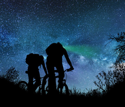 Couple ride bicycles at night under the milky way