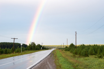 countryside road wet with rain and part of the rainbow over the road