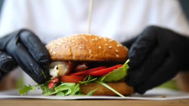 Hands In Black Gloves Holding Delicious Vegan Burger With Tofu And Vegetables. Close-Up.