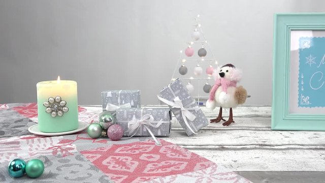 Die Kamera f&auml;hrt auf einem Slider entlang eines Holztisches. Darauf stehen pastell farbige Weihnachtsdekorationen. Eine t&uuml;rkise Kerze, graue Geschenke, ein Bilderrahmen mit dem Text: merry christmas.