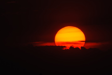 The setting red sun in front of a thick wall of clouds