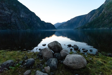 View over a Norwegian fjord with reflecting water and some stones in the foreground