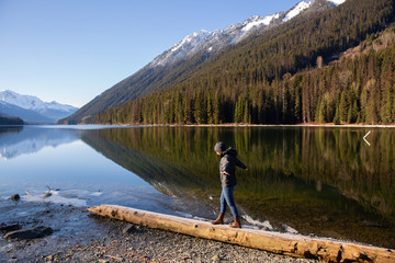 British Columbia Canada, Duffy Lake with smooth water reflection and mountains in backgrounds and woman walking balancing on log