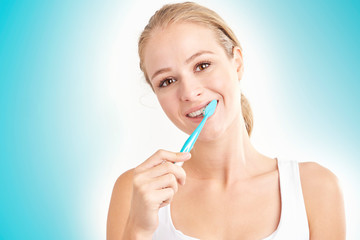 Studio shot of beautiful young woman brushing her teeth while looking at camera and smiling....