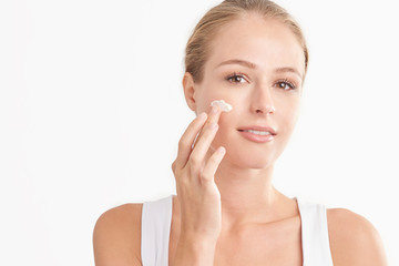 Young woman applying face cream against white isolated background
 