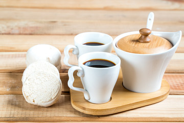 Marshmallow with marmalade, jug of milk, coffee in cup and sugar, spoon on wooden table