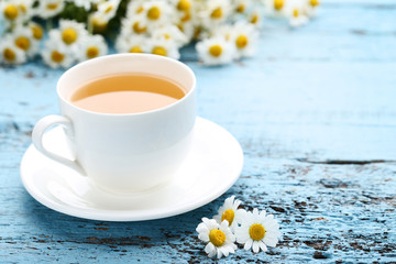 Cup of tea with chamomile flowers on blue wooden table