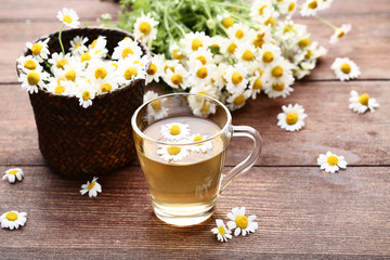 Cup of tea with chamomile flowers on brown wooden table
